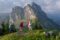 Drei Personen wandern auf einem Hügel, im Hintergrund sind massive Berge zu sehen.